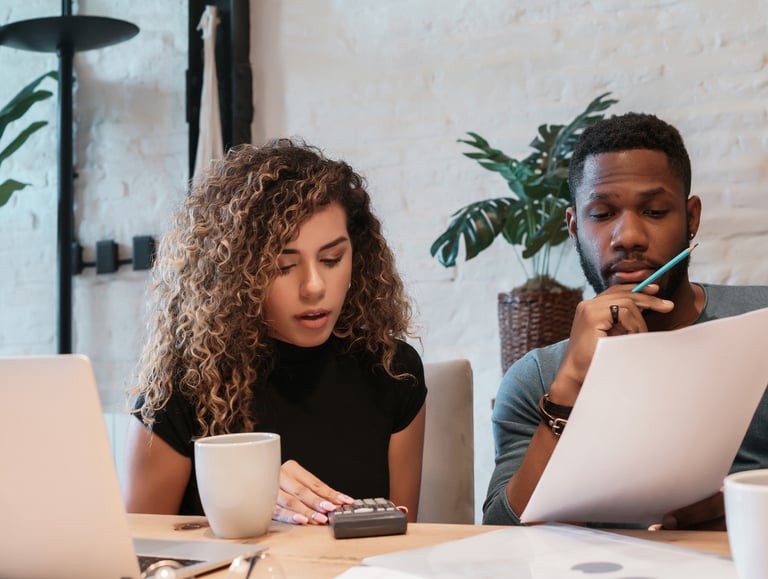 Young couple reviewing financial documents and using a calculator to plan their household budget at home.