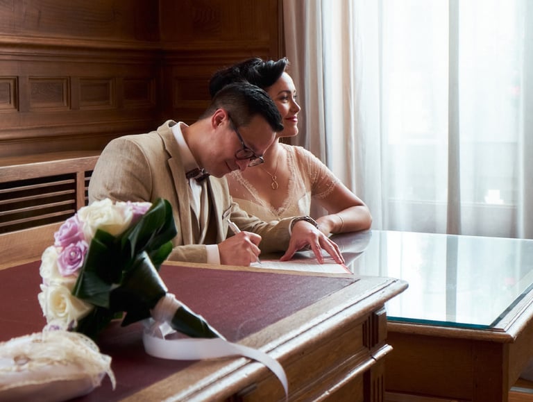 Couple de mariés signant leur acte de mariage et un bouquet de fleurs au premier plan.