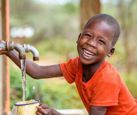 a young boy is smiling and holding a cup of water