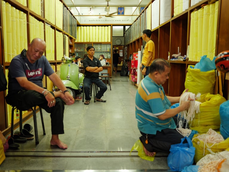 Men seated working in a textile shop in Chinatown, Bangkok, By ACAT Photos.