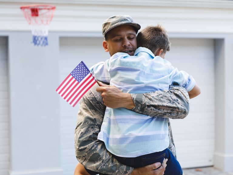 a veteran in uniform carrying his son and holding a us flag