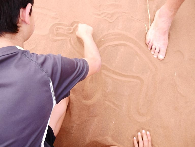 A boy draws a picture of a camel in the sand while on a desert tour in the Sahara