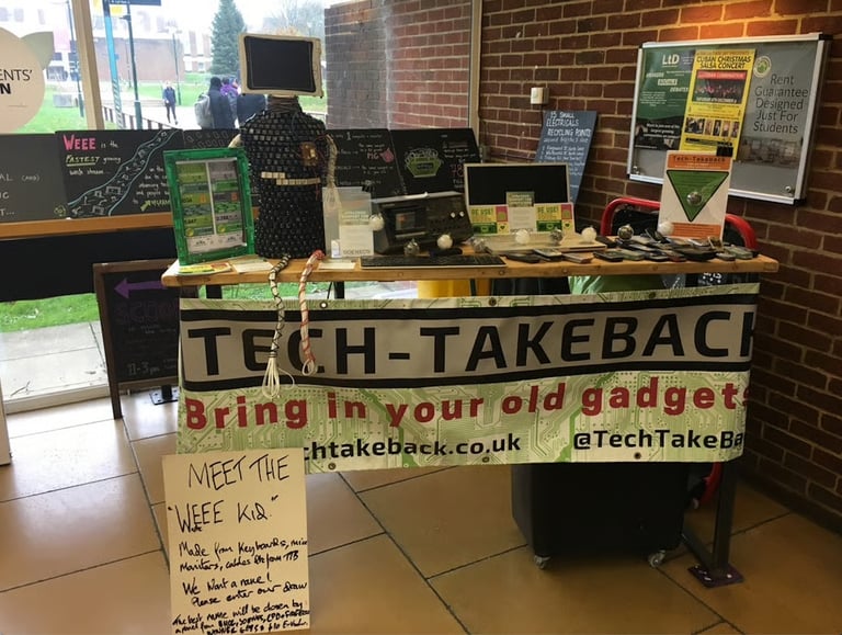 A photo of the first Tech-Takeback pop-up. A home-made banner hangs from a table covered in old tech