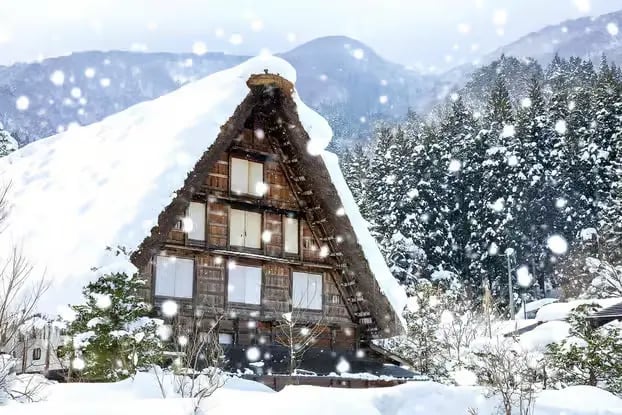 Heavy snow falling on a traditional Gassho-style farmhouse roof.