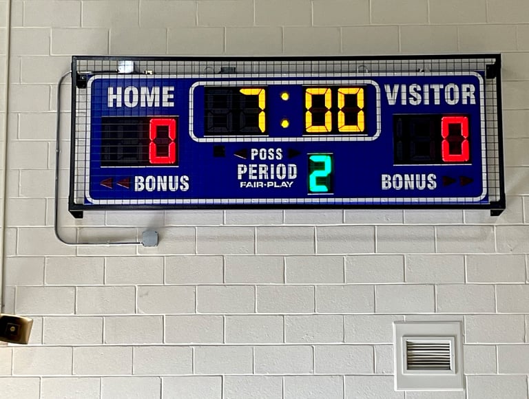 Scoreboard with protective wire mesh screen mounted on a gym wall