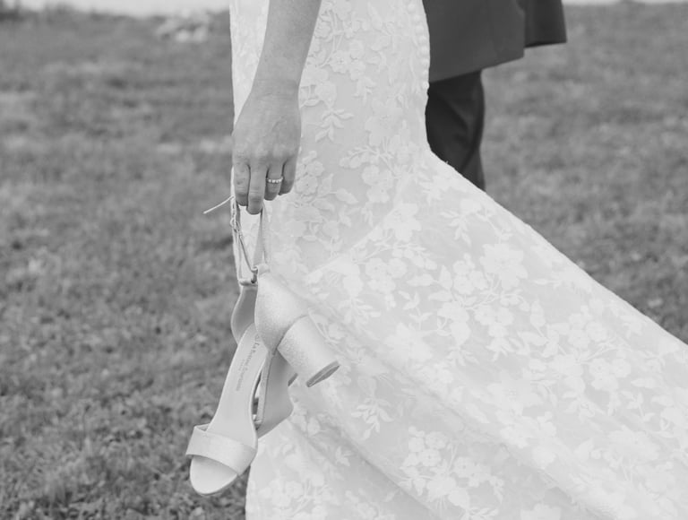 Mariée tenant ses chaussures de mariage à la main lors d'un moment de détente en extérieur