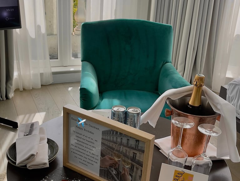 a table with a bottle of champagne, card, cake, macaroons, dessert, and framed letter