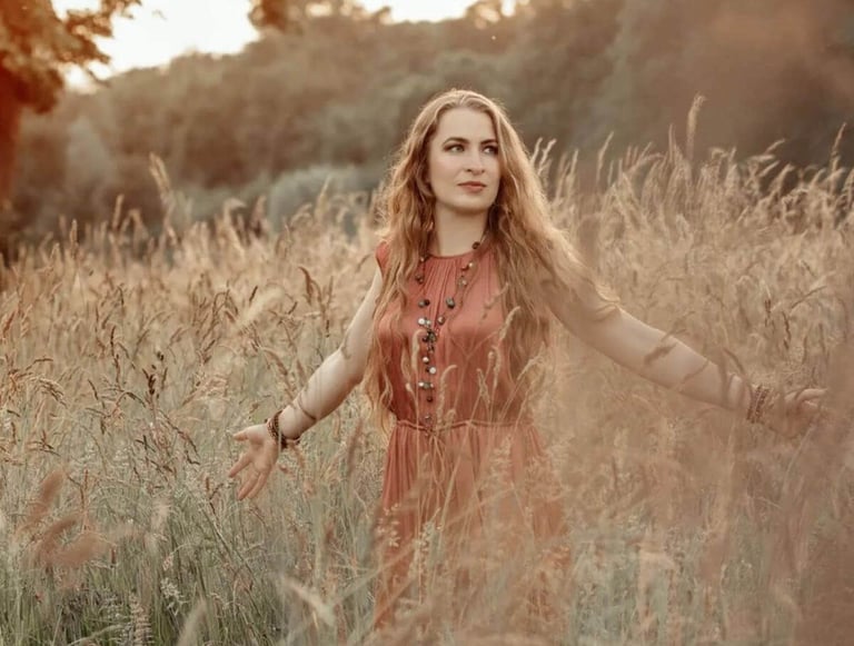 Trauerrednerin Leonie Stratmann steht im altrosanen Sommerkleid in einem Feld mit Wildblumen, hinter ihr Wald.