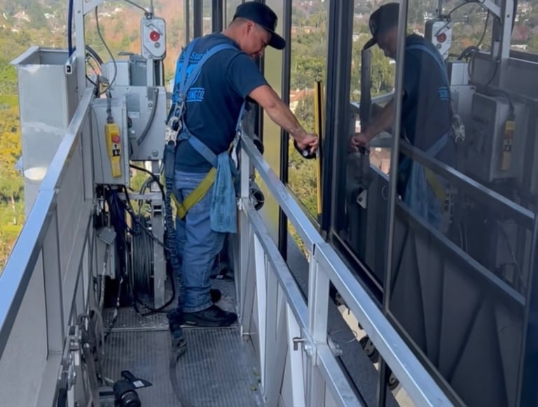 Professional window cleaner in safety harness using a squeegee on high-rise office windows from a platform.