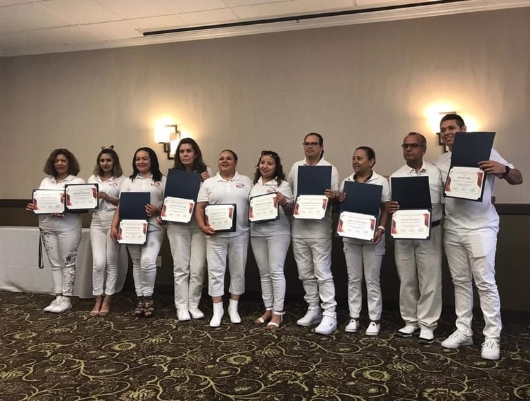A group of diverse professionals in white uniforms holding graduation certificates and award folders.