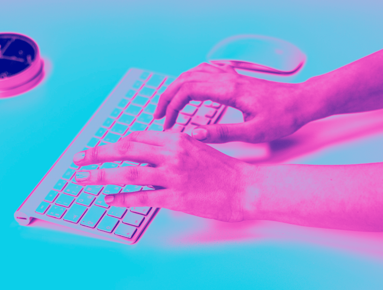 Hands typing on a wireless computer keyboard under vibrant pink and blue neon lighting.
