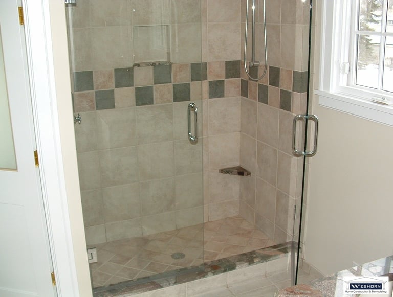 Walk-in shower featuring glass doors, neutral porcelain tiling, and a decorative mosaic border.