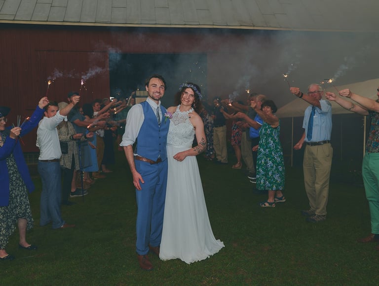a bride and groom are standing in front of a barn with guests holding up sparklers
