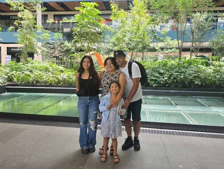 A happy family posing together in a modern outdoor shopping center with lush green plants.
