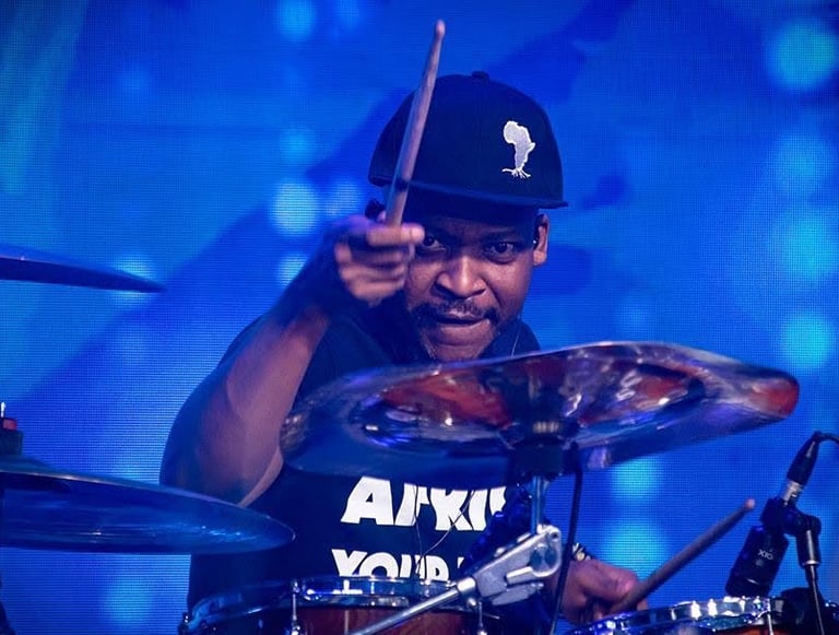 Guy wearing a cap, lifting a stick and playing drums