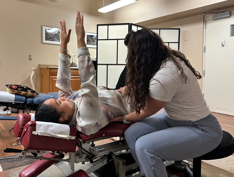 Chiropractor with hands on patients stomach and lower back, coaching form for rehab exercise.
