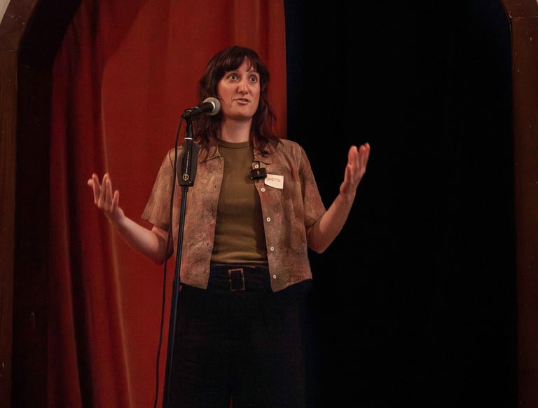 Young confident woman behind microphone speaking to audience using hand gestures