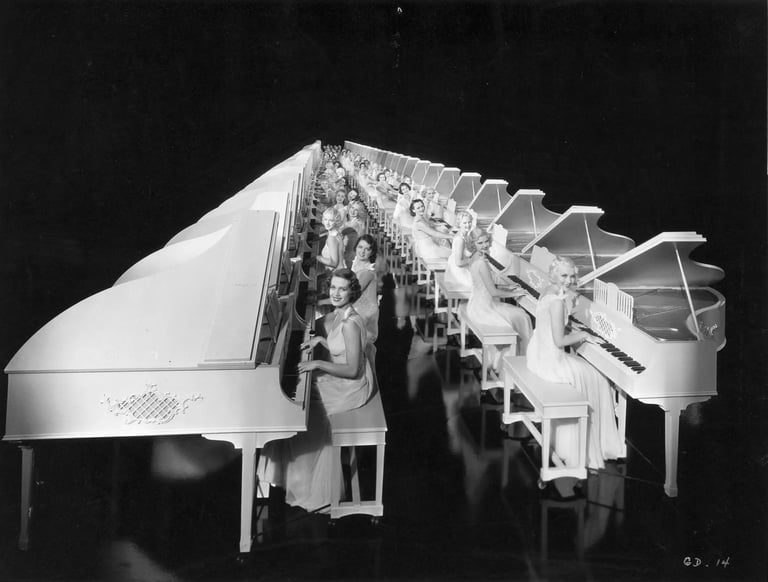 Regimented rows of white grand pianos played by chorus girls in white costumes, forming an endless l
