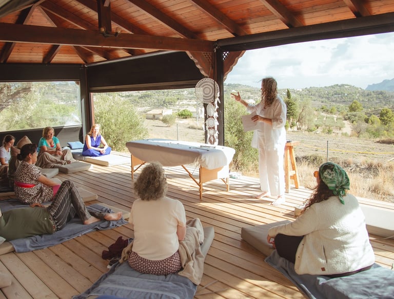 Sheila Doerfler in white linen explaining what a group biofield tuning session is to 9 people seated in Spanish country side