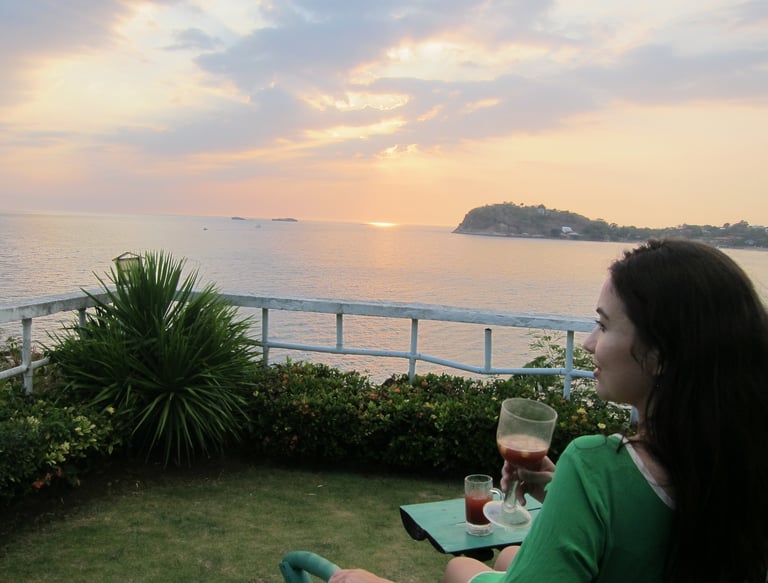 a woman sitting on a lawn chair with a glass of wine overlooking the ocean