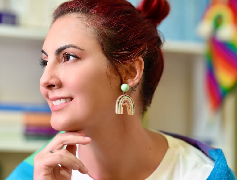 Retrato da psicóloga Palloma D'Andrade, frente a sua biblioteca com a bandeira Orgulho LGBTQIA+