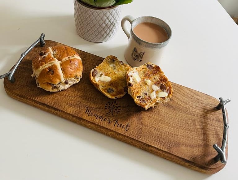 a wooden serving board with hot cross buns and a cup of tea