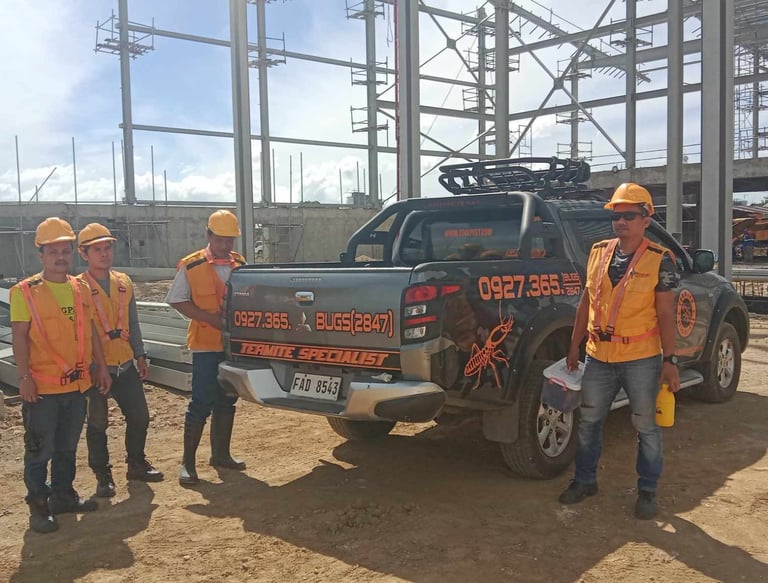 Termite specialist team in safety vests standing by a pest control truck at a construction site.