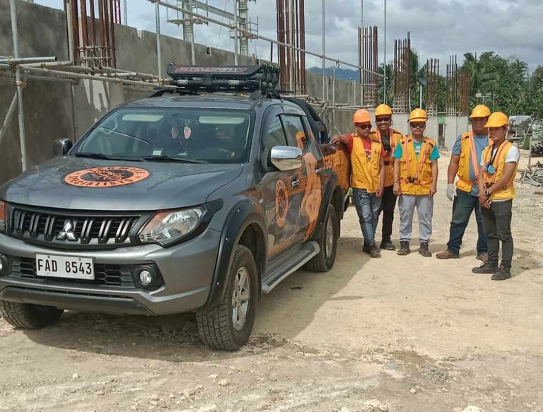 exterminators in safety gear standing by a Mitsubishi Triton pickup truck at a building site.