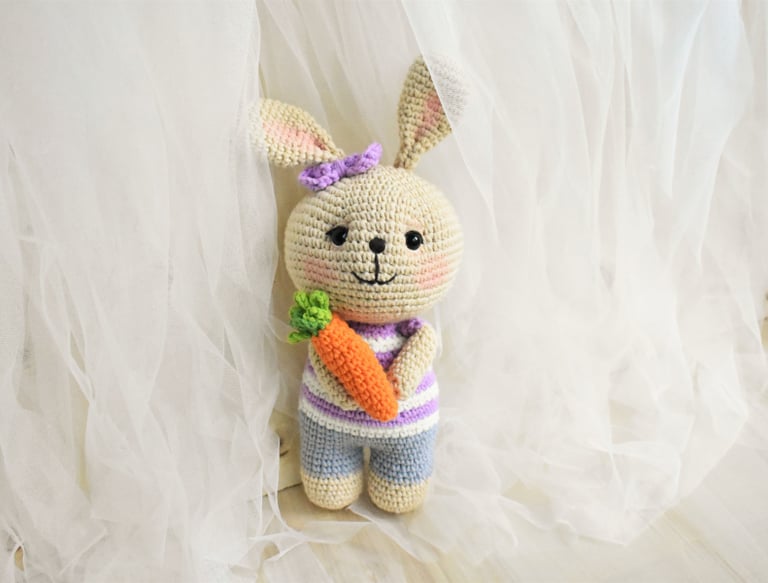 Conejo amigurumi tejido a crochet hecho a mano con camiseta morada a rayas sosteniendo una zanahoria