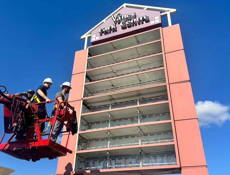 Technicians in a lift bucket performing maintenance on a tall commercial pylon sign at Valley Park Centre.