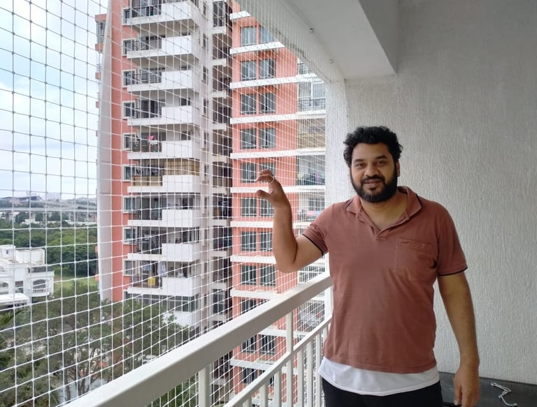 Happy family standing safely behind a newly installed balcony safety net in a Bengaluru apartment.