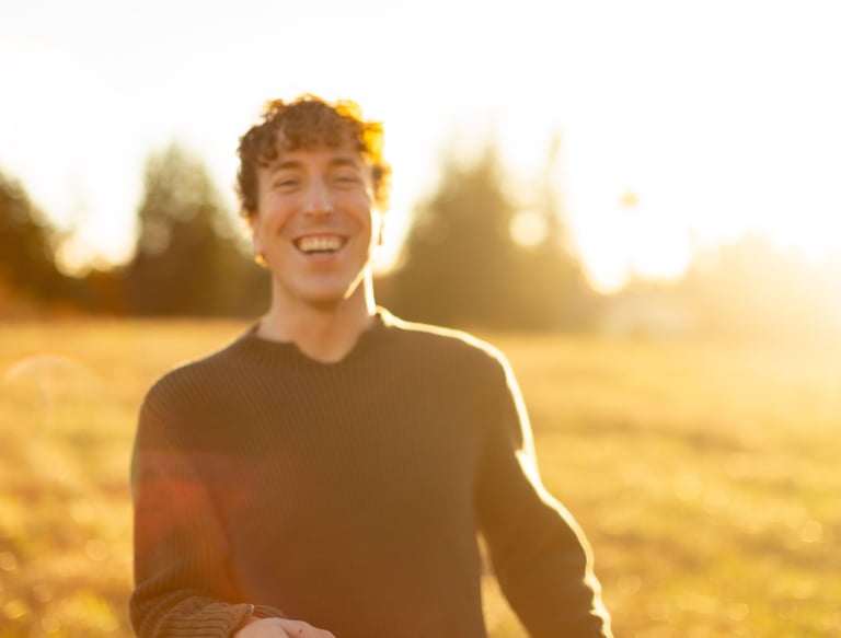 A happy man with curly hair laughing in a golden sunlit field during sunset.