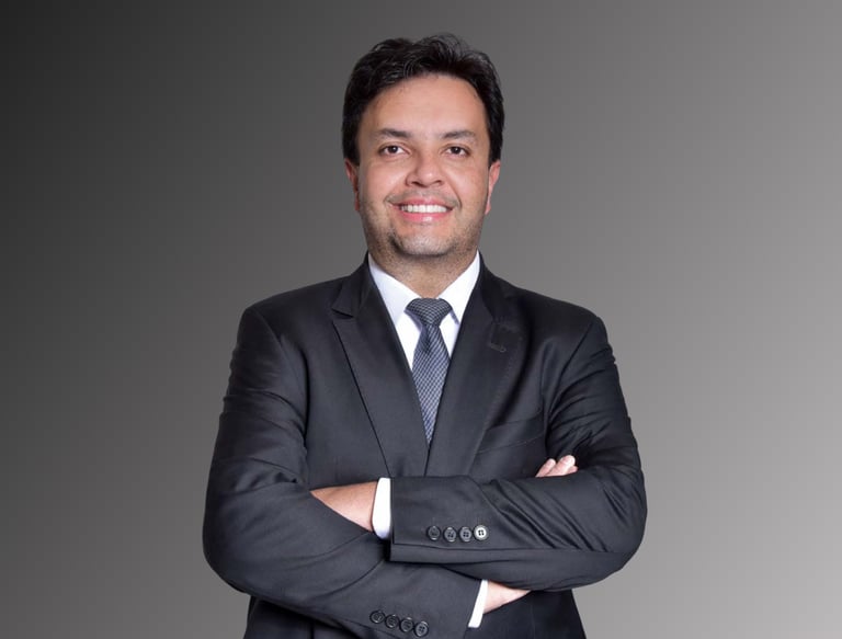 Professional corporate headshot of a smiling businessman in a black suit with arms crossed.