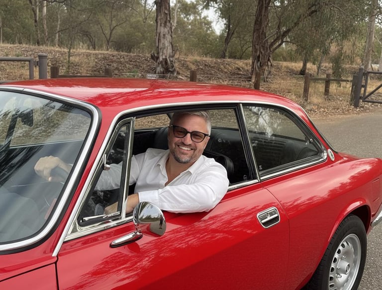 Image of a man sitting in a red 1974 Alfa Romeo smiling at the camera