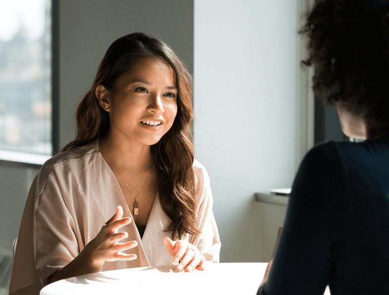 two women of color sitting at a table talking to each other