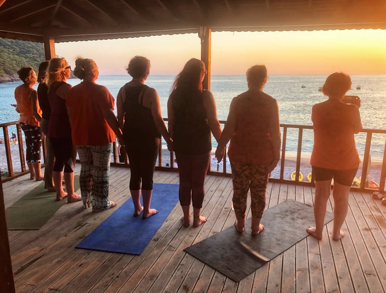 A goup of women holding hands and looking out to sea as the sun sets in the Kabak Valley