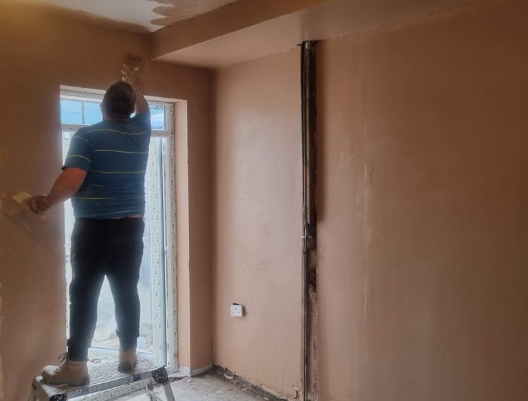 Professional plasterer applying fresh plaster to a room ceiling and walls during a home renovation.