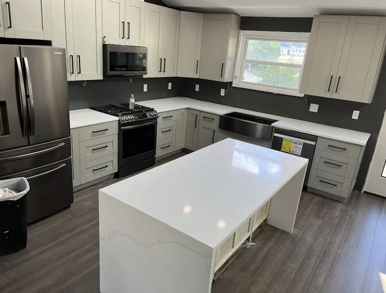 A newly renovated modern kitchen with light gray cabinets, white quartz countertops, stainless steel appliances, and a