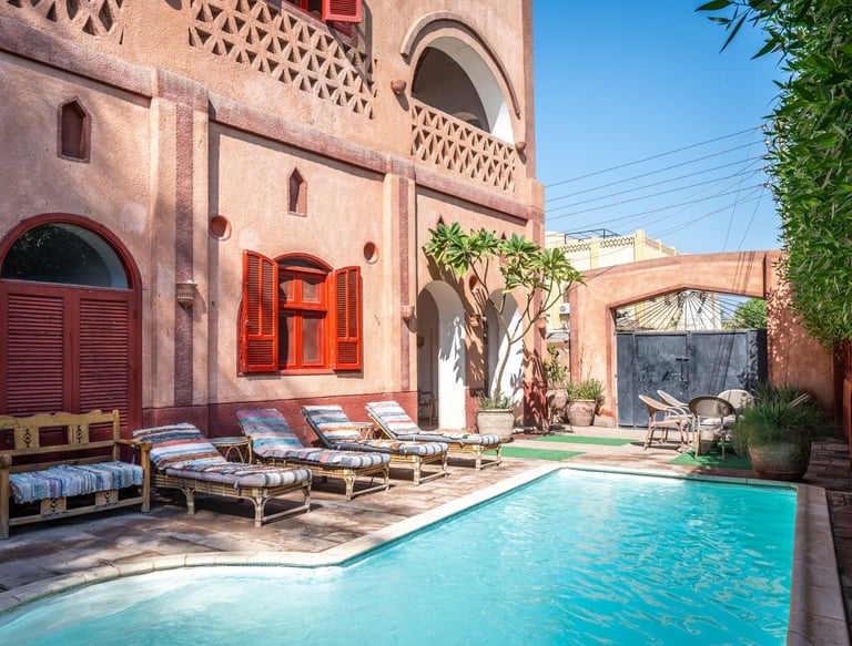 Luxury terracotta villa courtyard featuring a turquoise swimming pool and striped lounge chairs.