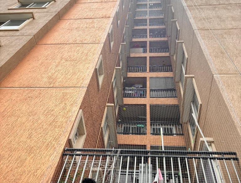 A wide shot of a balcony in Mumbai with Arjilli Safety Nets installed, sunlight casting shadows thro