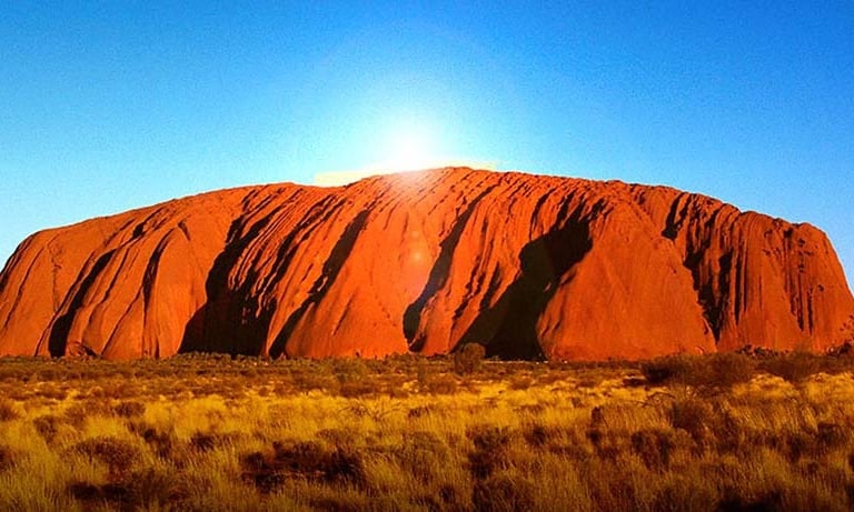 Sun glowing over Uluru, a majestic red sandstone monolith in Australia's Northern Territory.