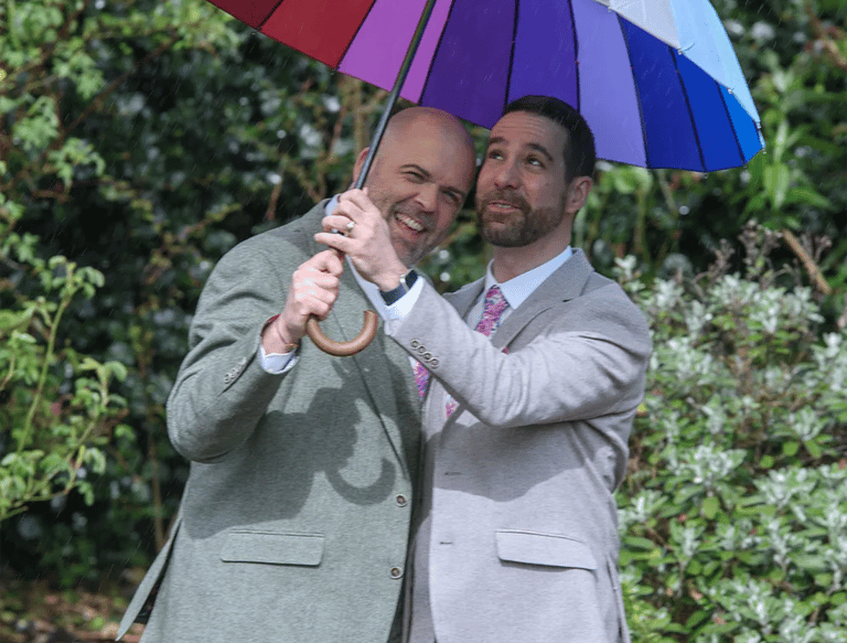 LGBTQ+ wedding couple under their rainbow umbrella