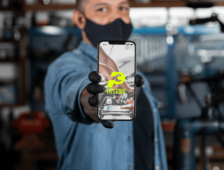 Auto mechanic holding a smartphone showing the Pitstopr mobile app for car repair services.
