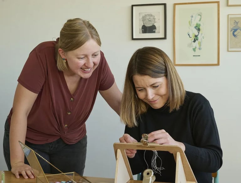 Dos mujeres sonrientes creando joyería artesanal hecha a mano en un estudio creativo con luz natural