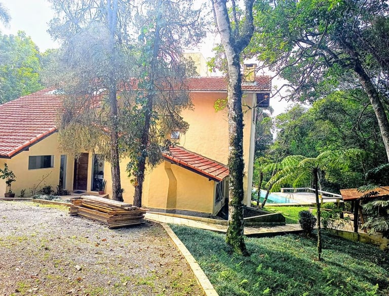 Vista do refúgio com múltiplos telhados, estacionamento, piscina e churrasqueira integrados à mata.