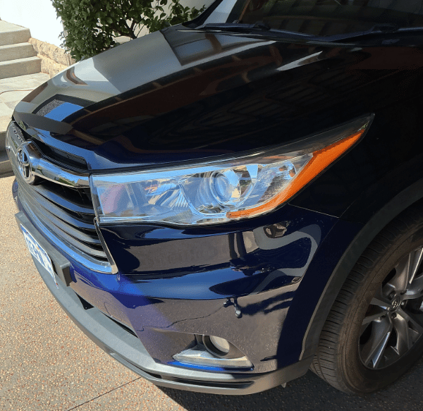 Close-up of a blue Toyota SUV headlight and front bumper in a driveway.