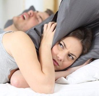 Donna si copre le orecchie con un cuscino mentre il suo compagno russa a letto.