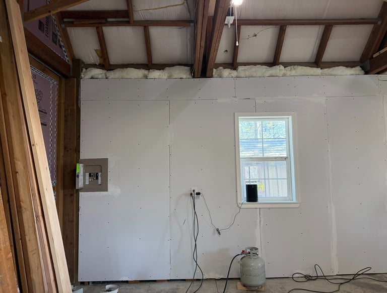 Interior garage renovation showing newly installed drywall, window, and electrical panel.