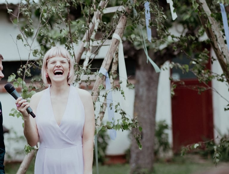 Traurednerin Silke lacht während einer freien Trauung und hält eine persönliche Rede mit Mikrofon im Freien.
