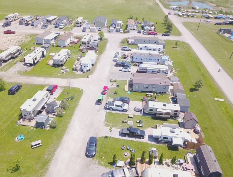 Aerial view of a sunny RV park with rows of campers, motorhomes, and parked cars on gravel lots.